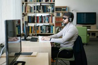 Blind man using headphones and Braille book by a computer